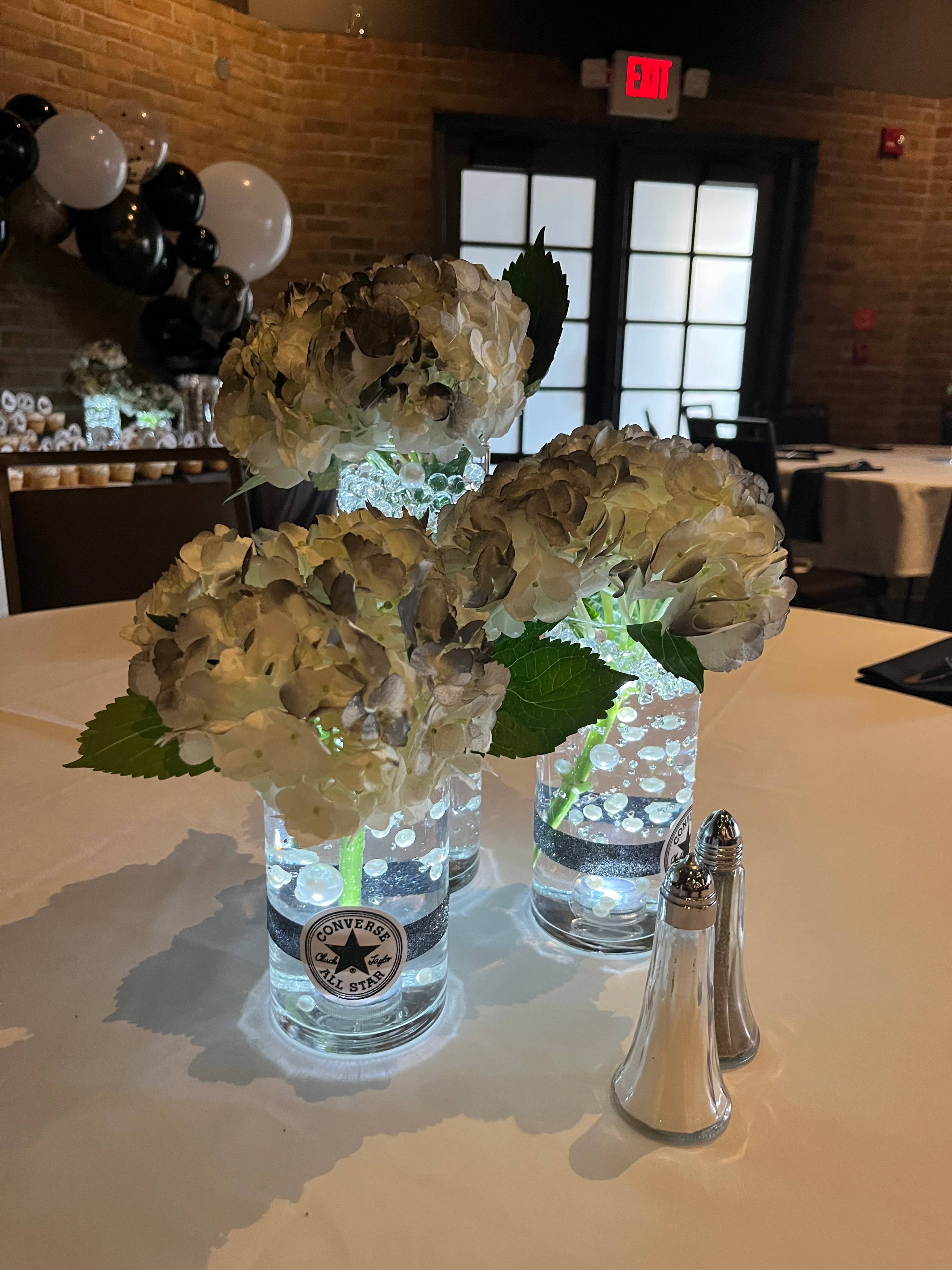 White hydrangea centerpieces in illuminated glass cylinder vases with Converse-themed black glitter bands at prom venue