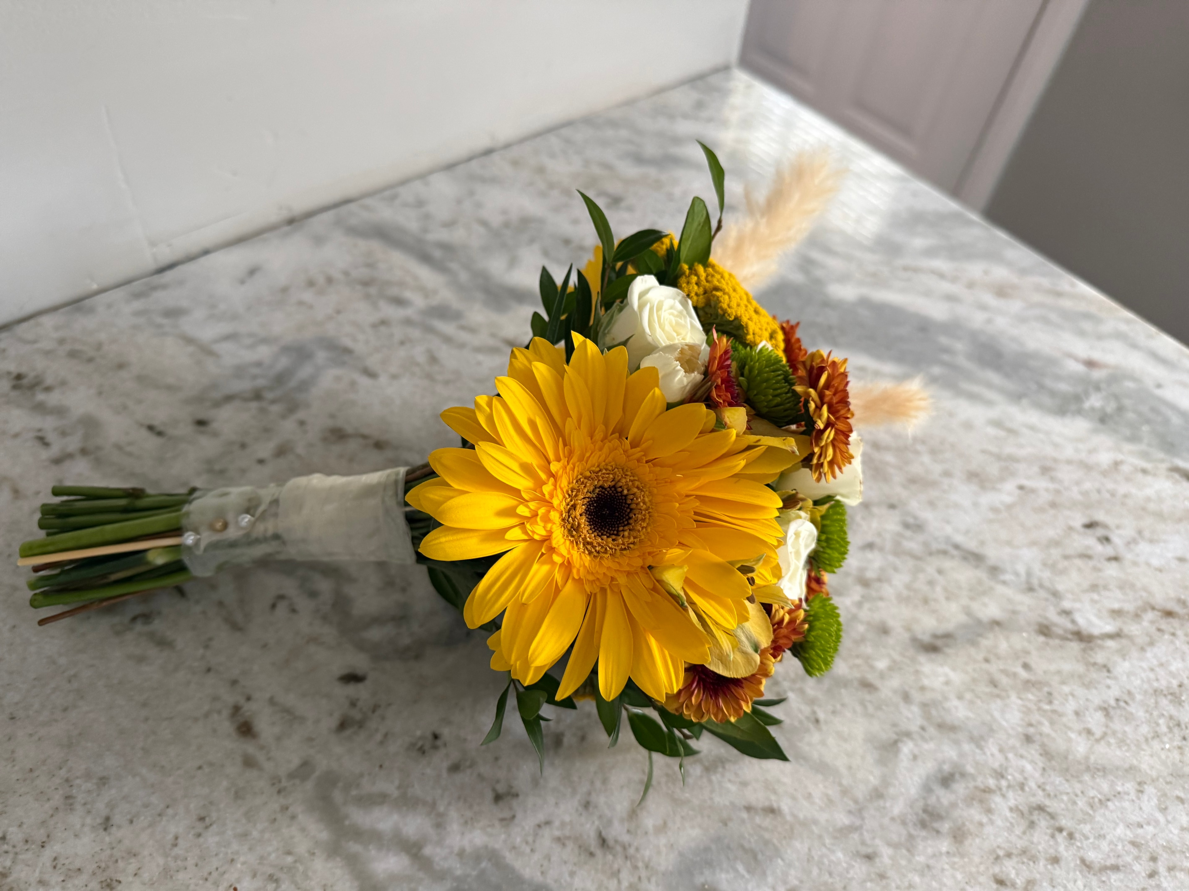 Yellow gerbera daisy and white rose bouquet with pampas grass and autumn mums on marble surface