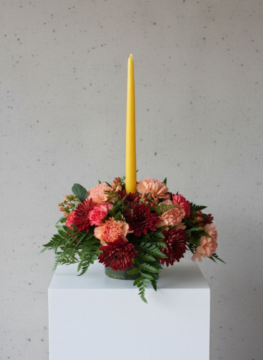 Autumn floral centerpiece with burgundy mums, peach carnations, and yellow taper candle on pedestal