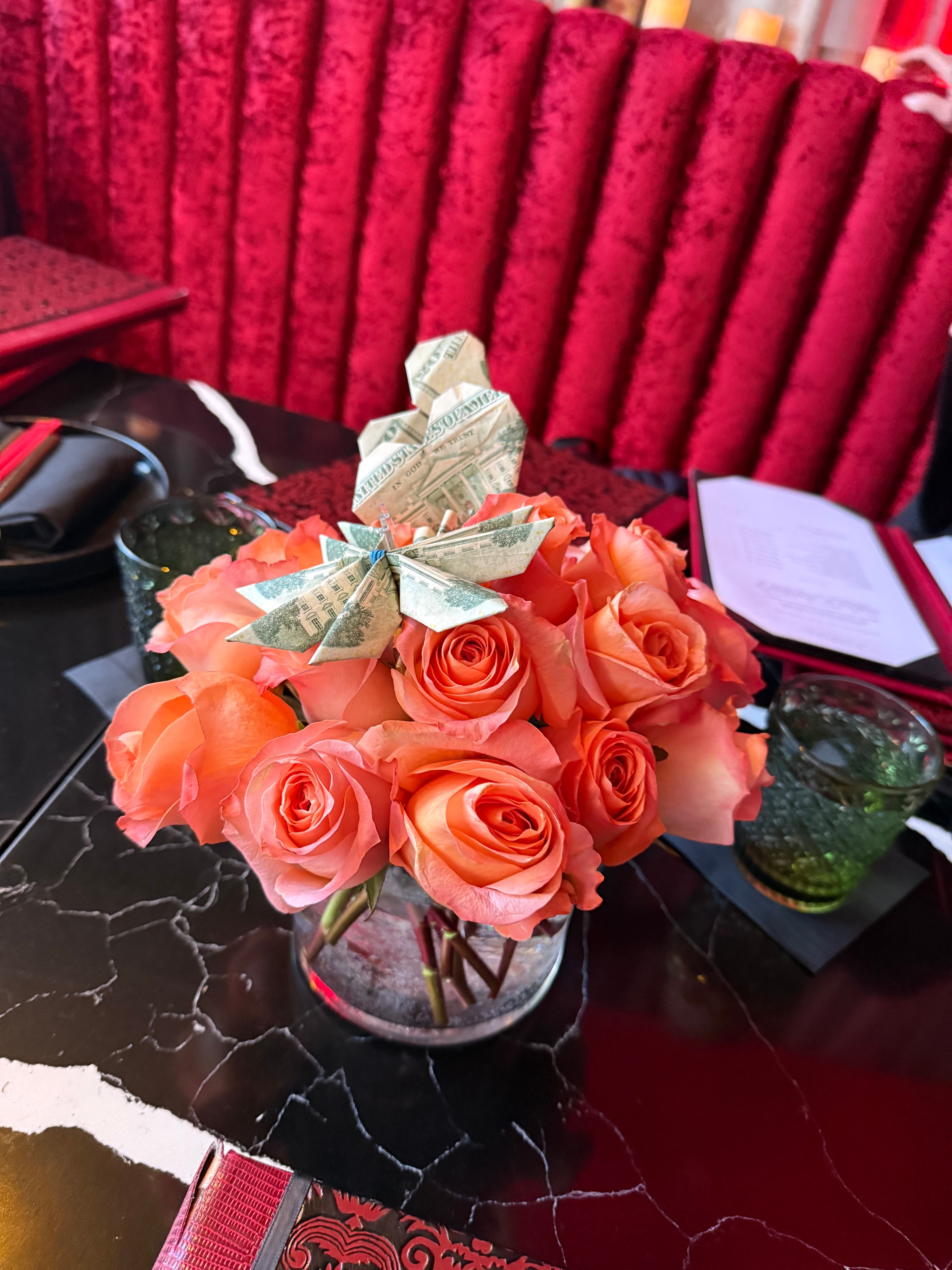 Coral roses with origami money butterfly accent in vase on marble table