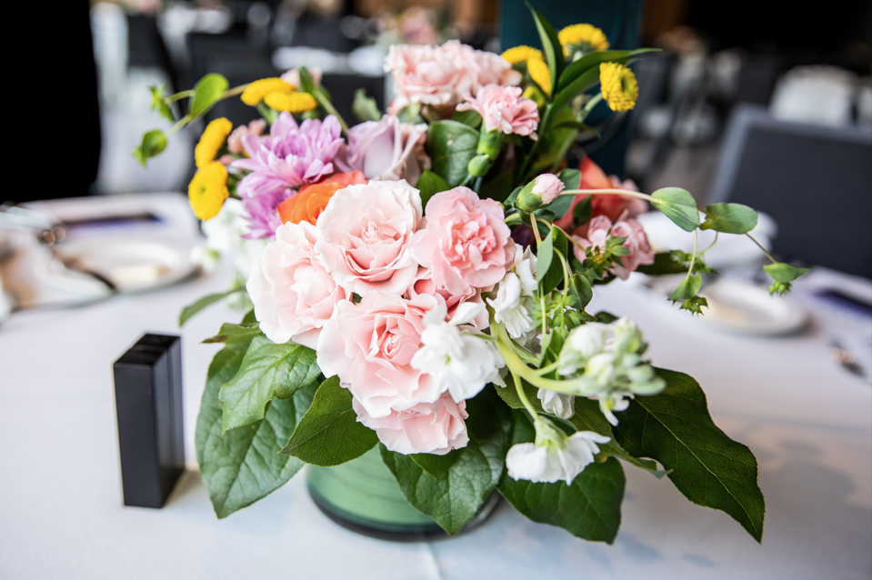 Pink roses, carnations, and yellow flowers in a green ceramic vase on a table