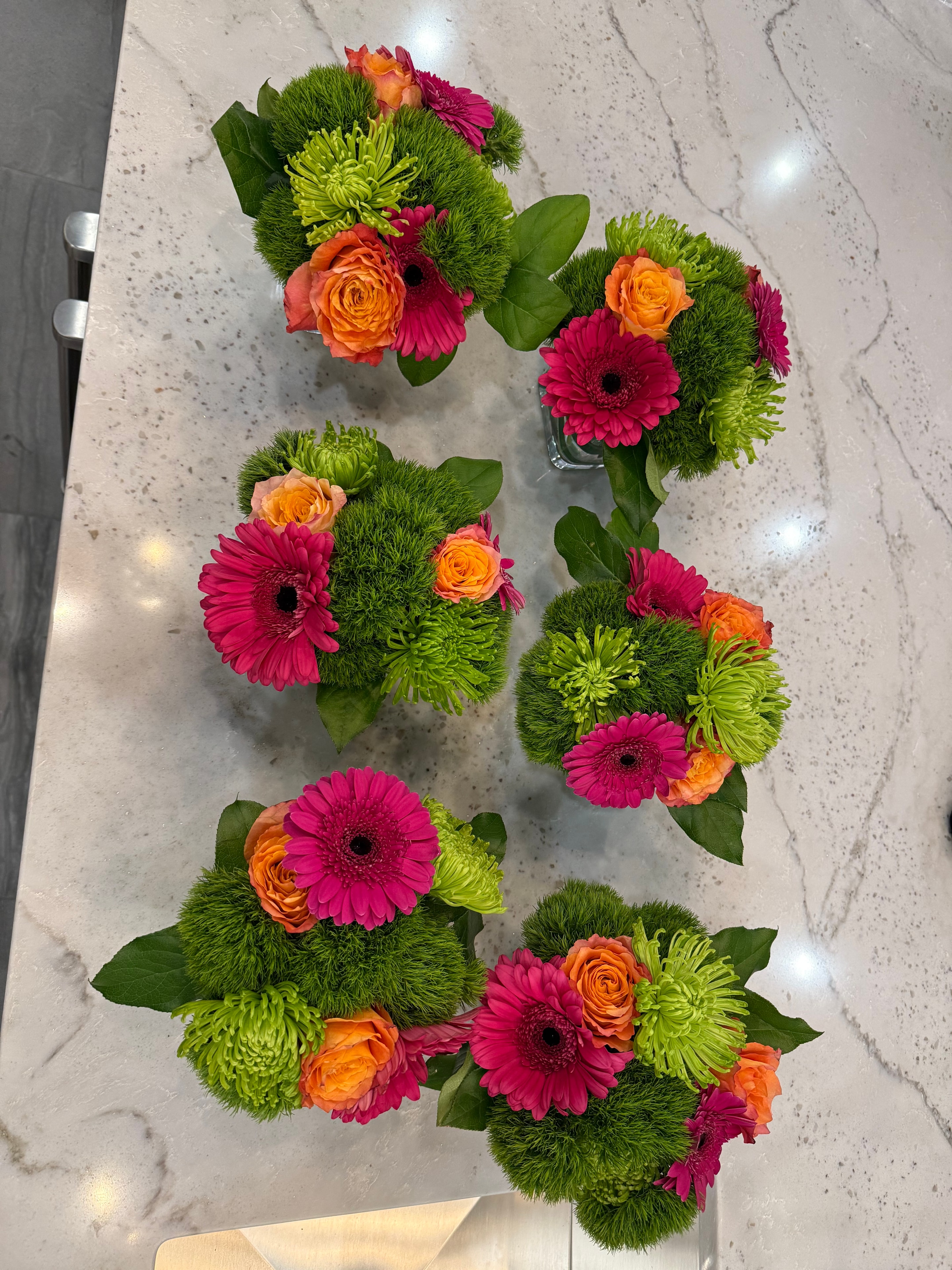 Six matching arrangements of orange roses, pink gerberas, and green chrysanthemums on marble